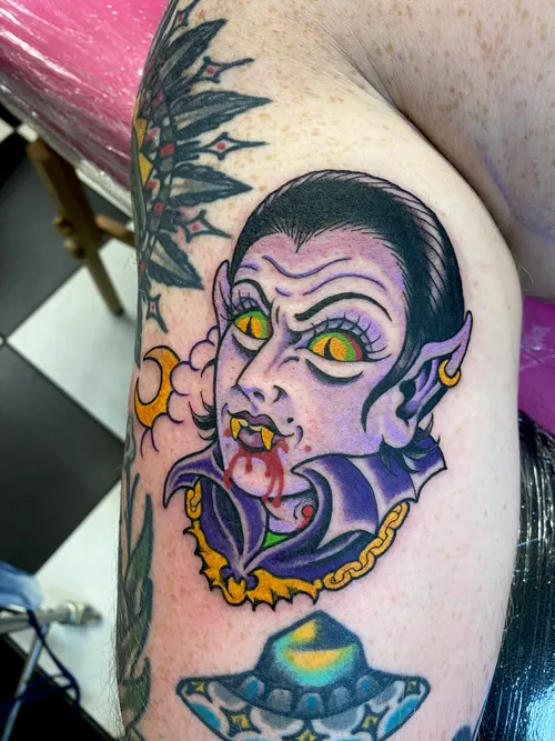 Purple old school vampire woman with glowing cat eyes and bloody fangs on the upper arm