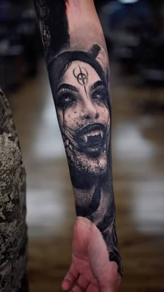 Black and gray forearm portrait of a fanged vampire with dark eyes and a third eye symbol