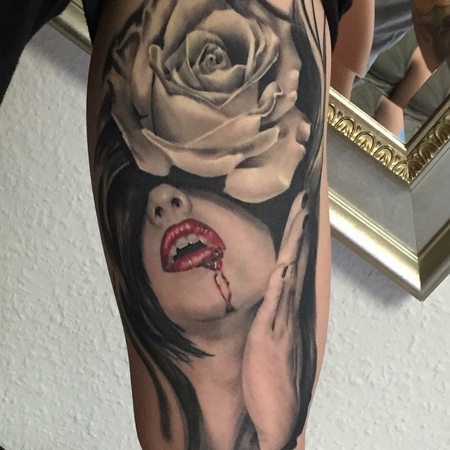 Fanged woman with bold red lips resting beneath a large rose as blood drops down her thigh