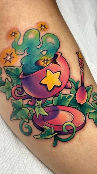 A pink cauldron witch tattoo with a glowing star, teal smoke, and ivy vines wrapped around the calf.