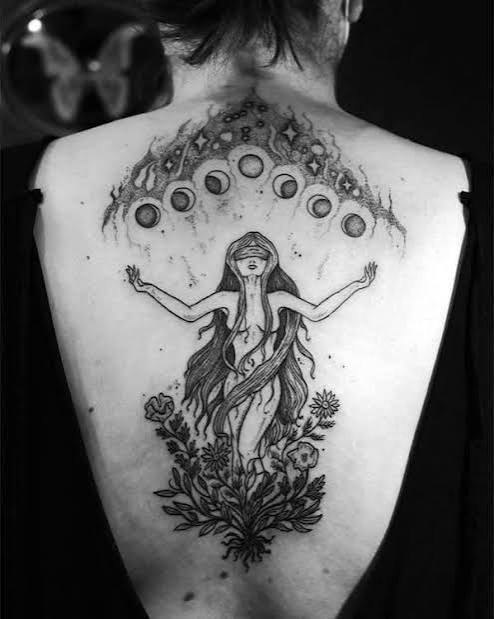 A blindfolded moon goddess witch tattoo with roots and flowers growing from her hair down the spine.