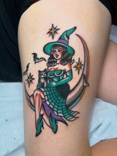 A pinup witch tattoo sitting on a crescent moon with her black cat, in bold traditional colors on the thigh.