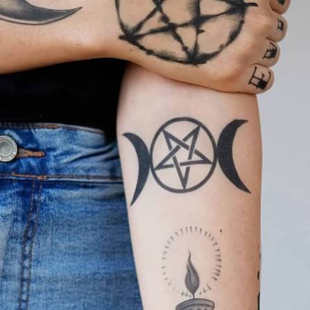 A triple moon pentagram tattoo with clean linework and a candle on the forearm.