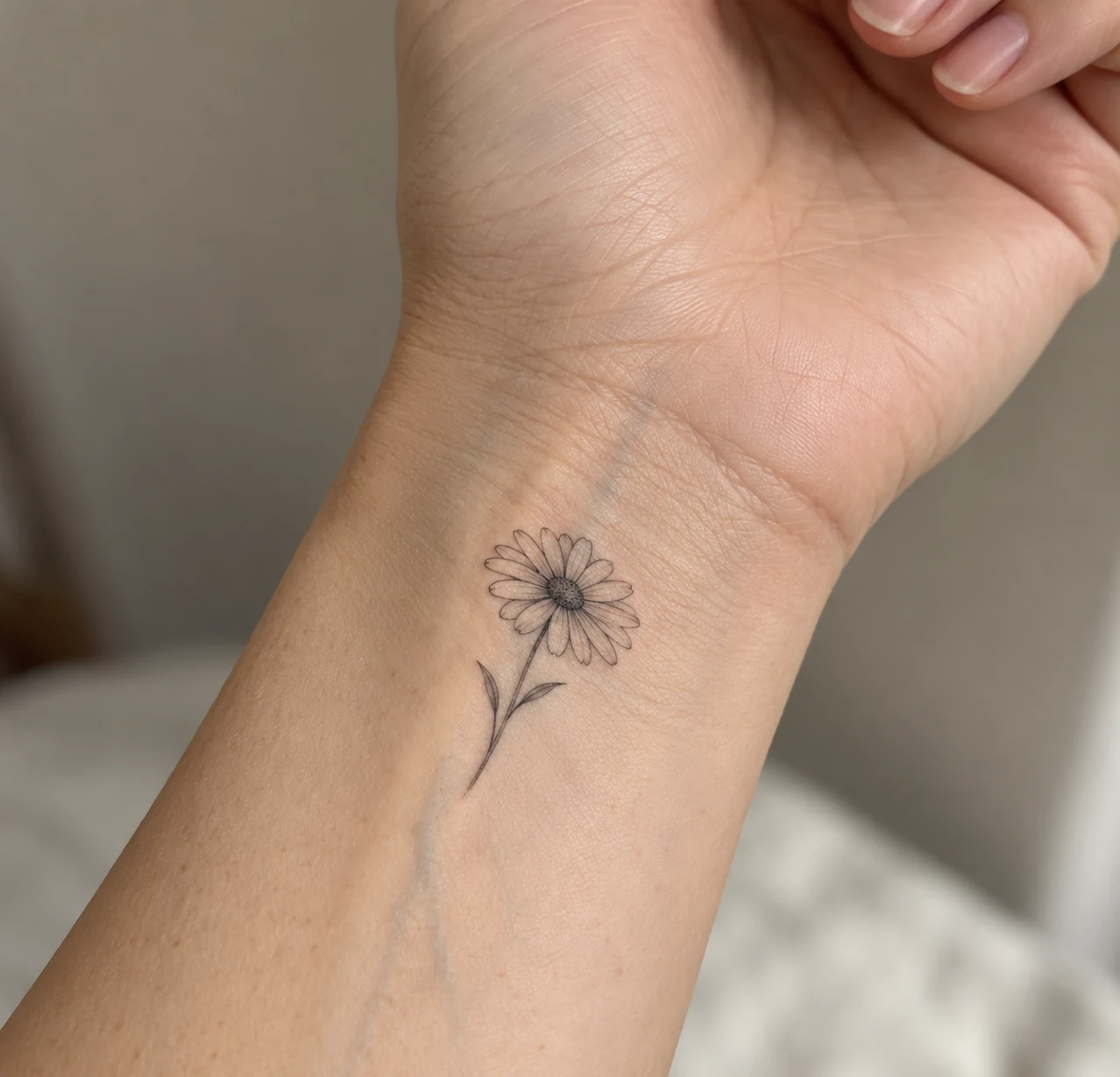Minimal fine line daisy tattoo on the inner wrist.