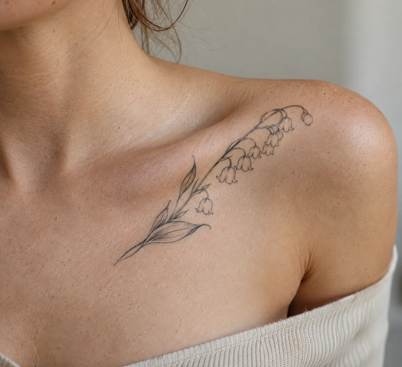 Fine line lily of the valley tattoo with hanging bell flowers along the collarbone.