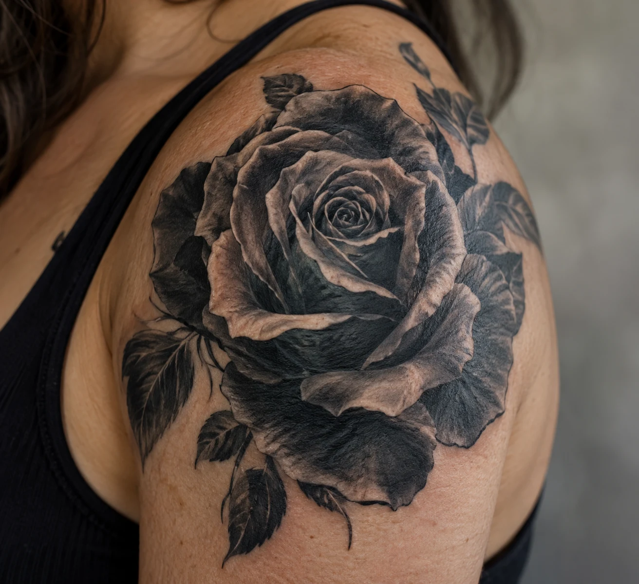 Black and grey rose tattoo with dark petals and shaded leaves on the shoulder.