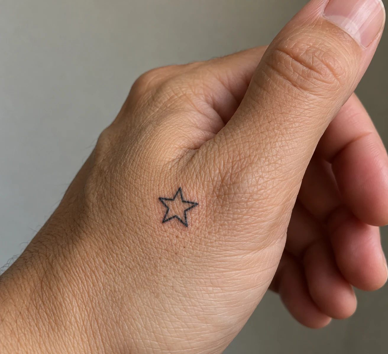 Small five-point outline star tattoo in black ink near the thumb base.