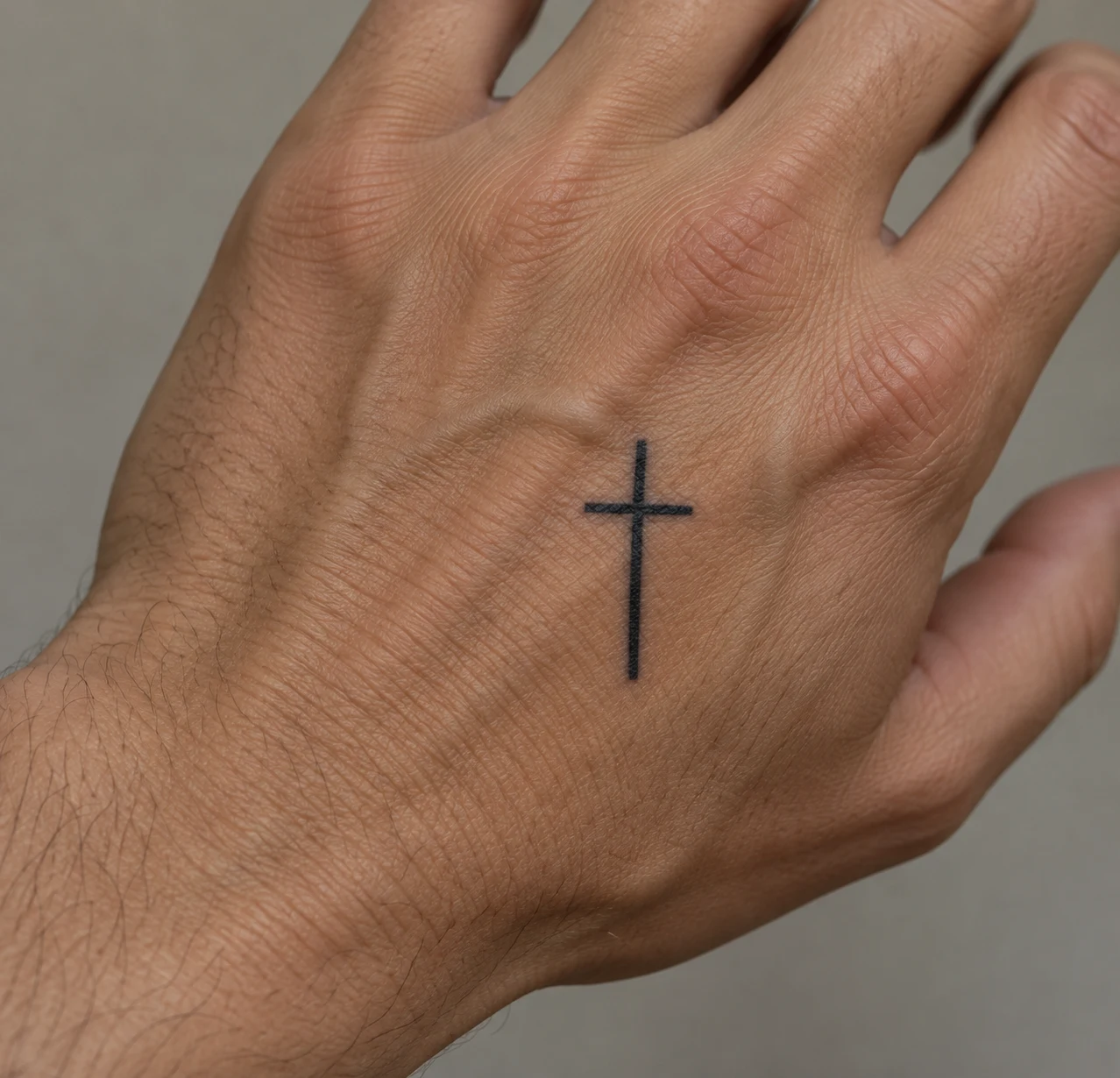 Simple black cross tattoo with straight lines on the back of a hand.