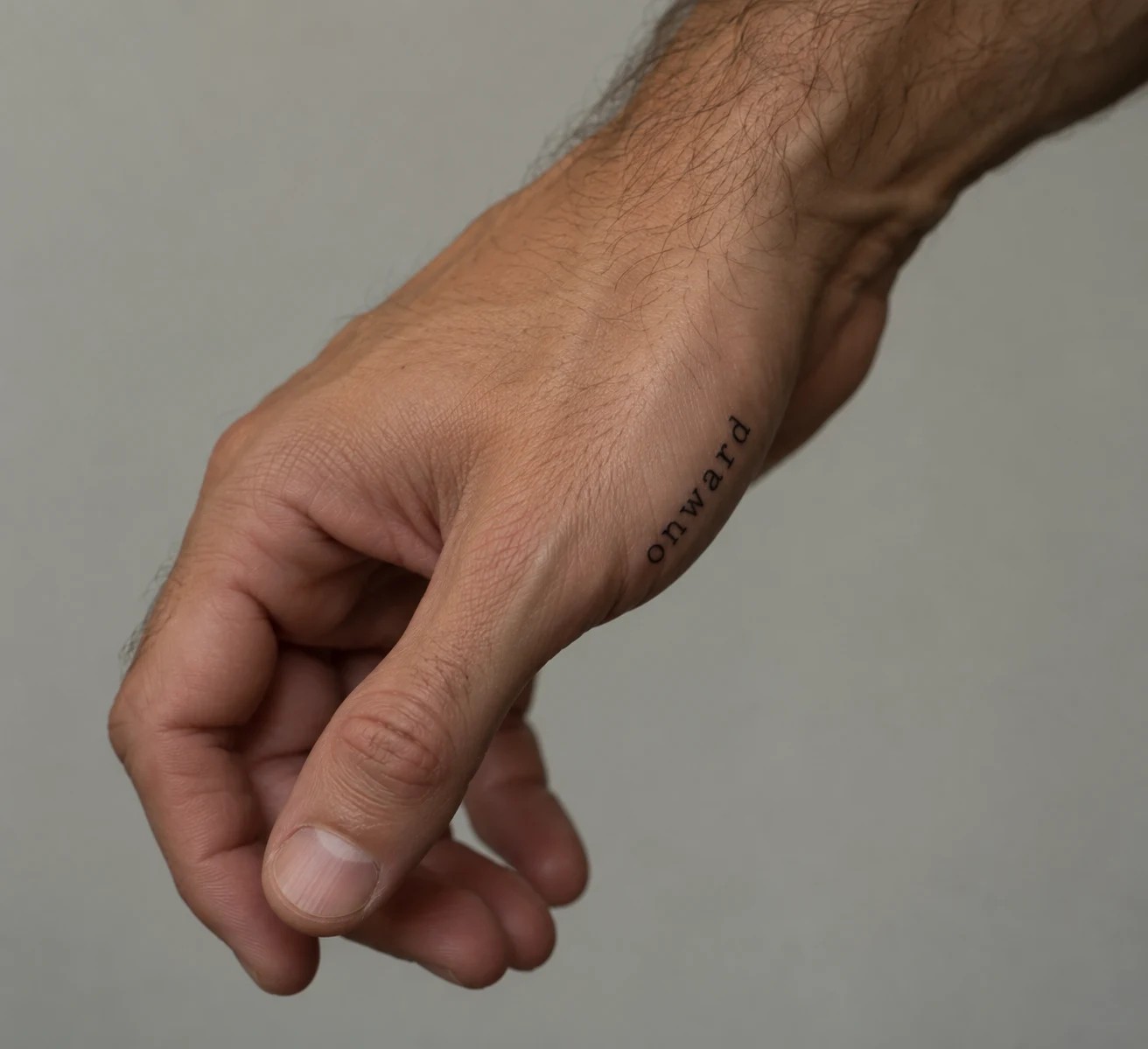 Black lettering tattoo reading “onward” along the outer edge of a man's hand.