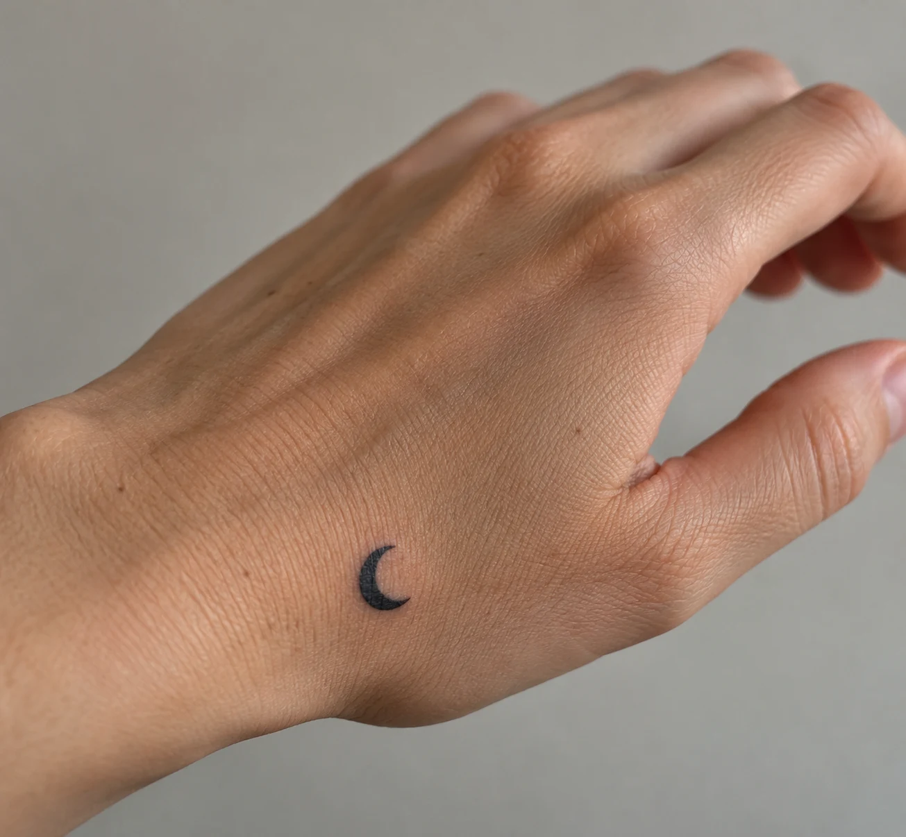 Small solid black crescent moon tattoo near the outer edge of the hand.